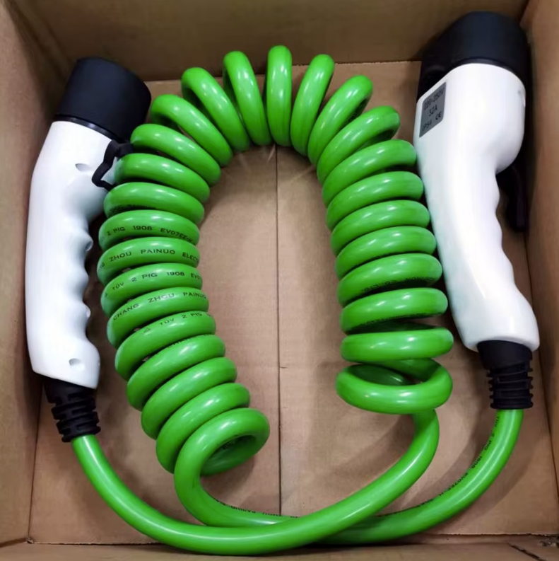 Câble de recharge vert enroulé en spirale, avec connecteurs blancs et noirs ergonomiques à chaque extrémité, soigneusement placé dans une boîte en carton ouverte. Le câble porte des inscriptions telles que 'ZHOU PAINUO ELECTRIC' et 'TUV 2 PIG 1908,' indiquant sa certification et ses spécifications pour une utilisation fiable dans la recharge des véhicules électriques