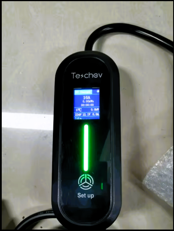 Une borne de recharge électrique avec un écran affichant des paramètres tels que l'intensité (16A), la consommation d'énergie (0.00kWh), et la température (17°C). Un voyant lumineux vert indique l'état de fonctionnement, et un bouton est visible sous l'écran