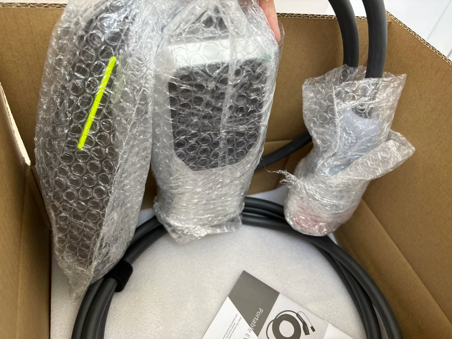 Chargeur portable pour véhicule électrique, soigneusement emballé dans du plastique transparent et placé dans une boîte en carton ouverte. Le chargeur est compact et pratique, idéal pour offrir une solution de recharge flexible et transportable, adaptée aux besoins des conducteurs de véhicules électriques.